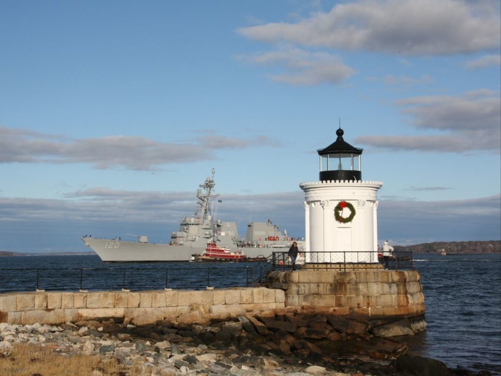 Bath-built Carl M. Levin (DDG 120) sails past a seasonally decorated Bug Light in Casco Bay during Acceptance Trials in December 2022.