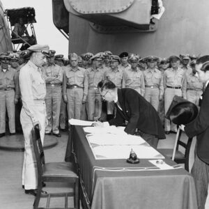 Japanese Foreign Minister Mamoru Shigemitsu signs the Instrument of Surrender on behalf of the Japanese Government, on board USS Missouri (BB-63), 2 September 1945. Lieutentant General Richard K. Sutherland, U.S. Army, watches from the opposite side of the table. Foreign Ministry representative Toshikazu Kase is assisting Mr. Shigemitsu. Photograph from the Army Signal Corps Collection in the U.S. National Archives.